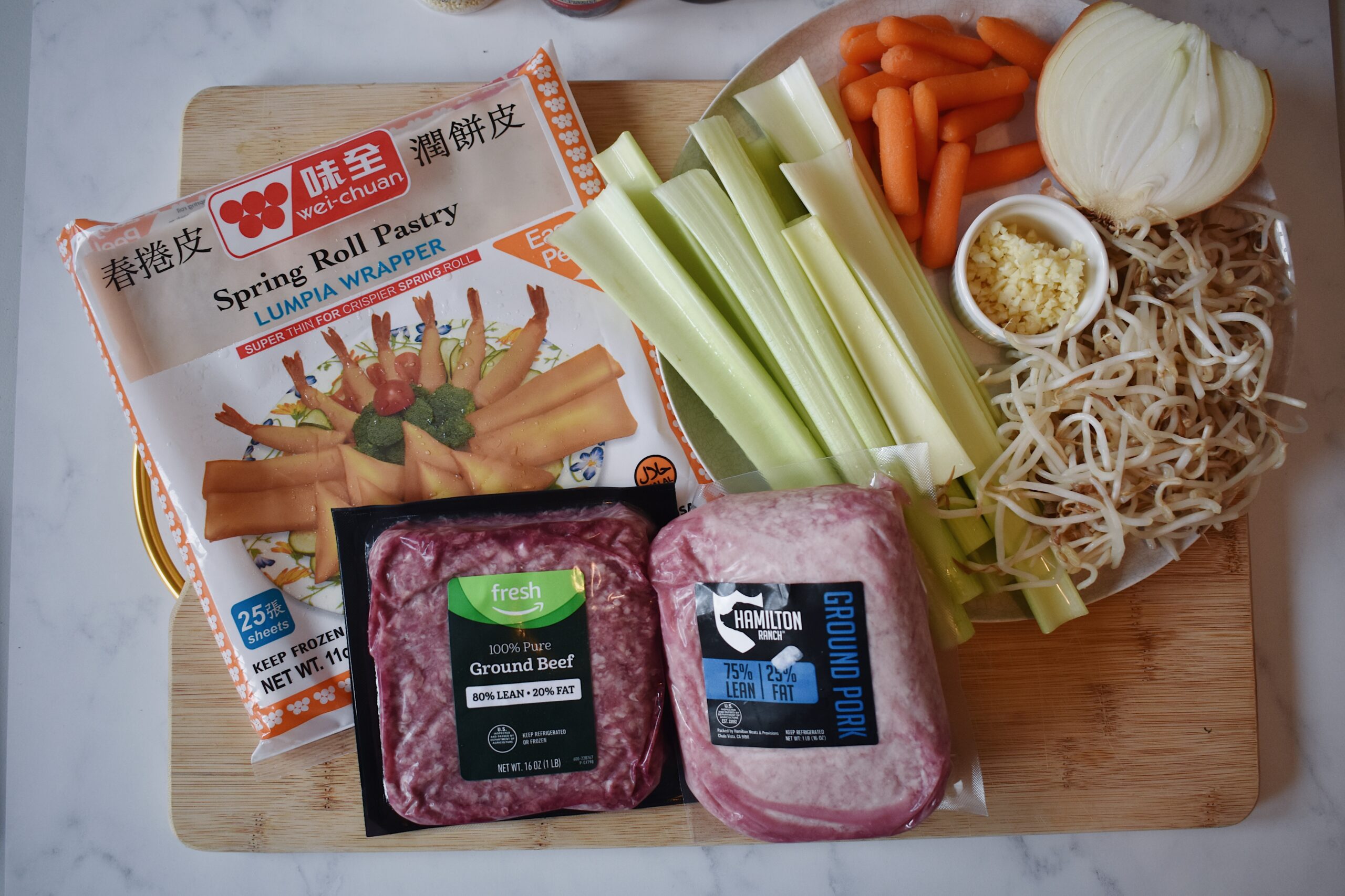 spring roll wrappers with pork and beef meat, celery carrots garlic onion and bean sprouts on a cutting board