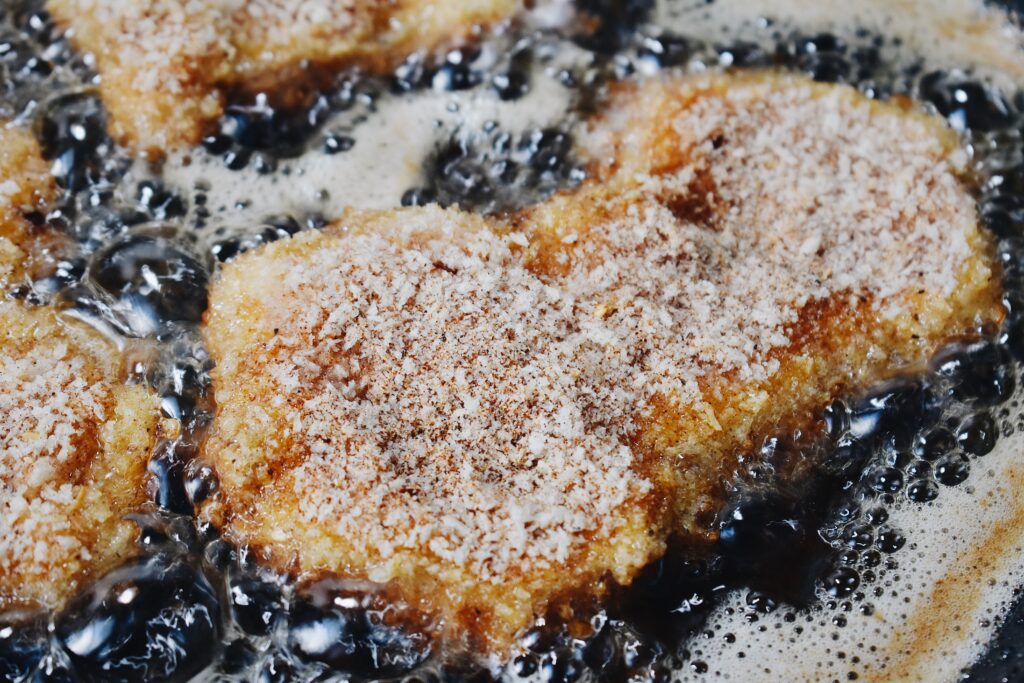 breaded chicken thighs frying in oil in a pan