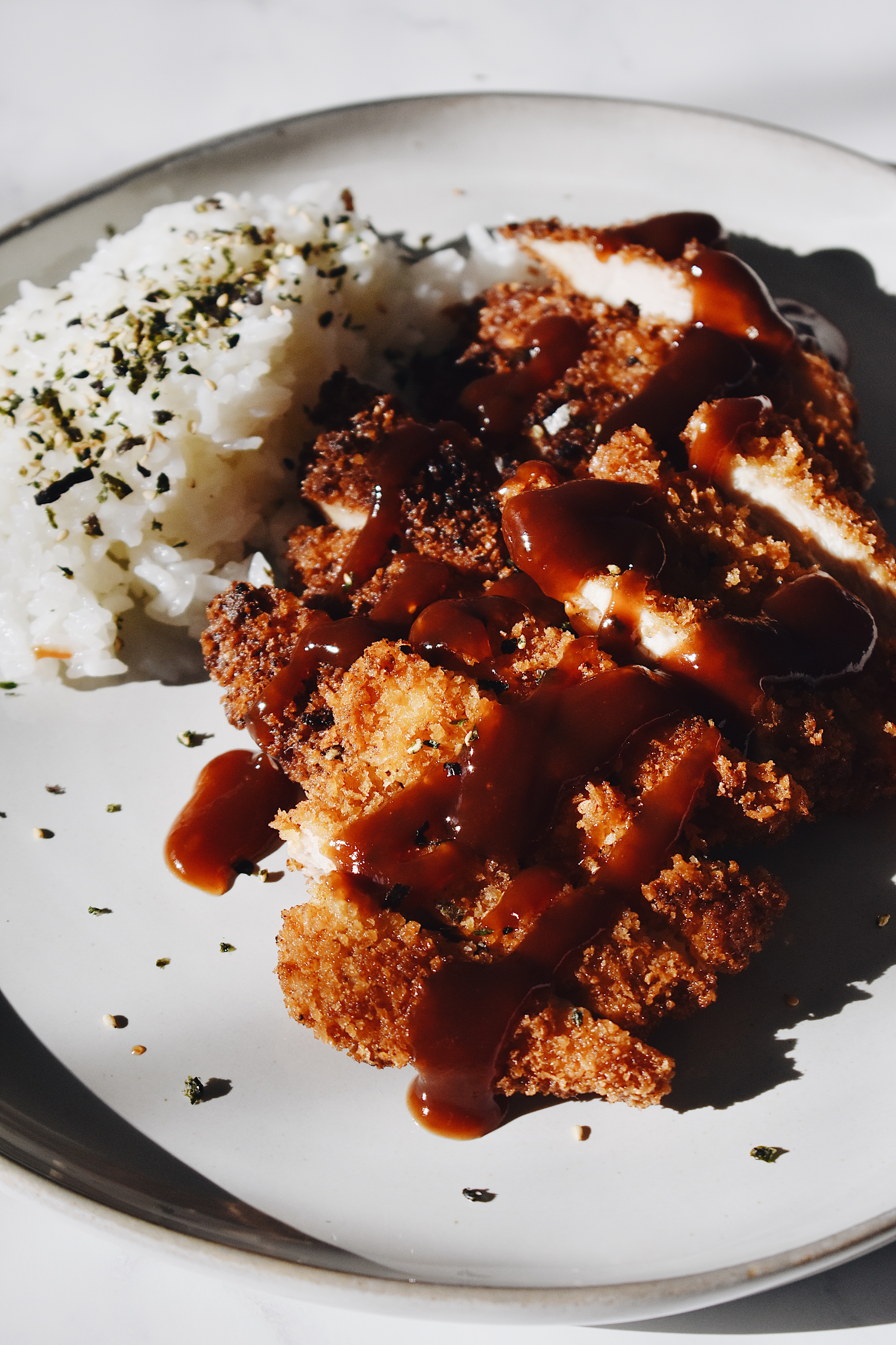 chicken katsu and rice on a plate in the sun with furikake on top and tonkatsu sauce on top