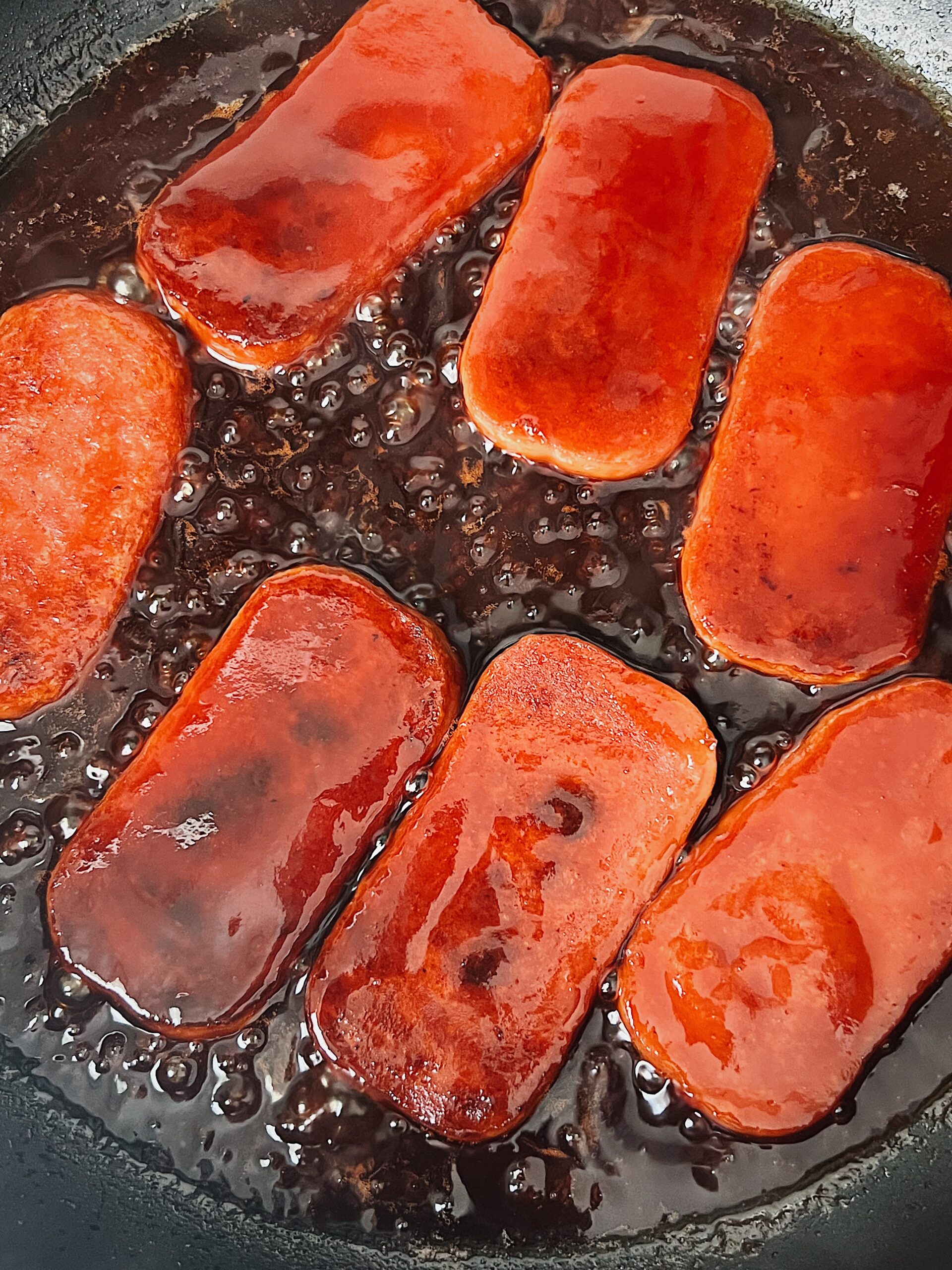 spam cooking in a pan on the stove covered in teriyaki sauce.