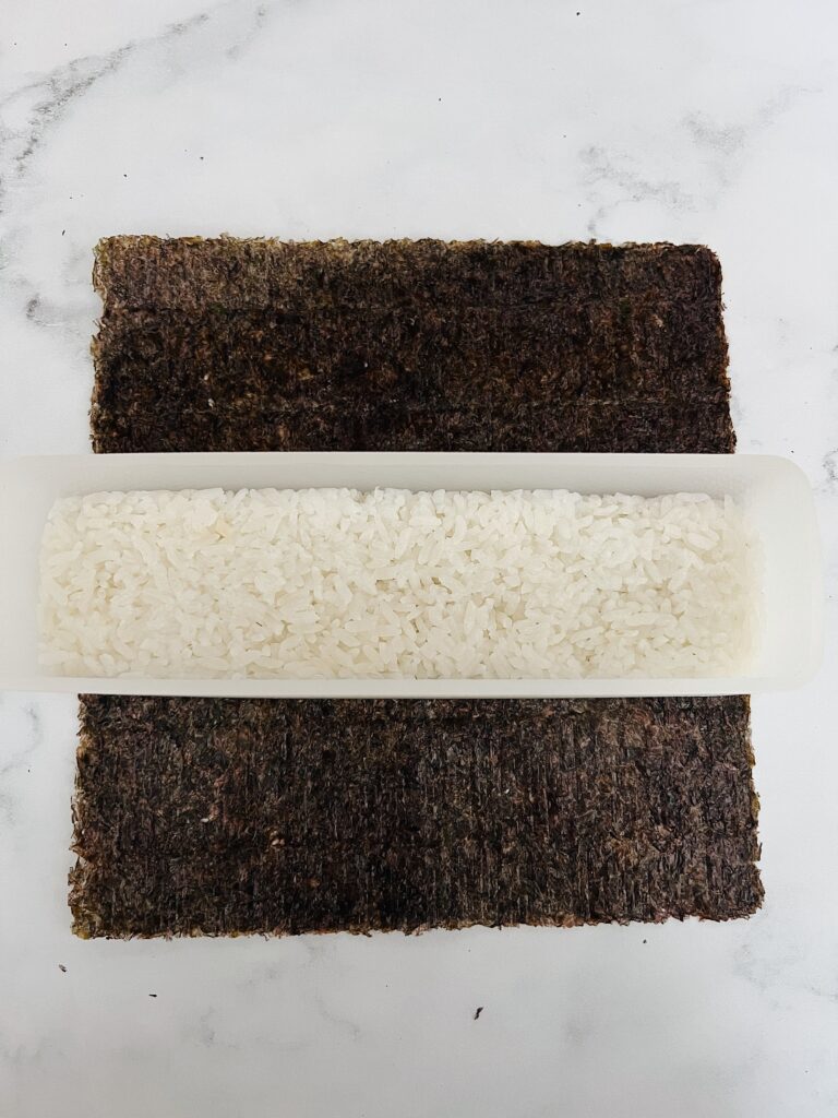 rice packed in a musubi maker on a sheet of nori.