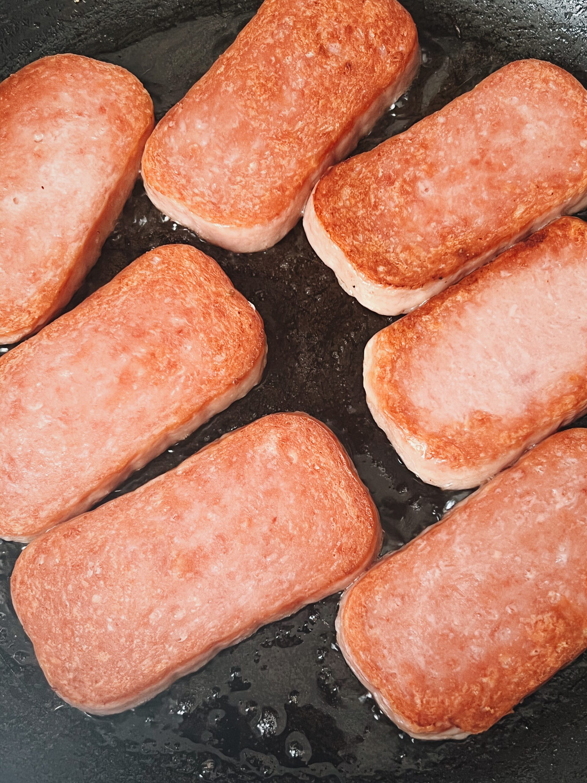 luncheon meat cut and being cooked until brown in a pan on the stove.