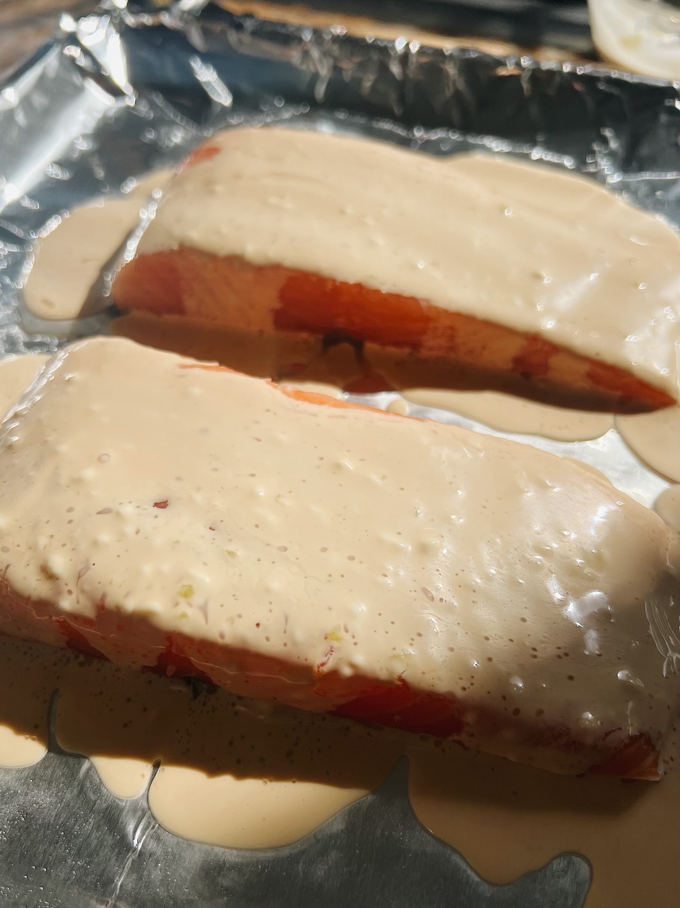 2 slabs of salmon on a baking sheet with foil. the salmon is covered in mayonnaise and soy sauce mixture.