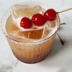 Mai tai mocktail in a glass with ice and 3 cherries on a toothpick as a garnish