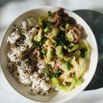 Kalua pig and Cabbage in bowl on the right half. Rice on the left half with Furikake and green onions on top.